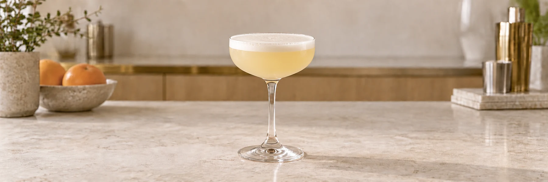 Akevitt Sour med hvitt eggehviteskum i et coupeglass på en lys bardisk